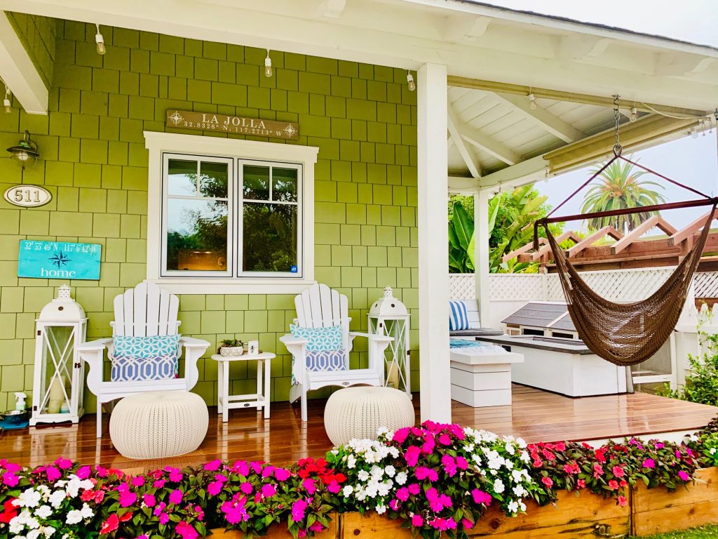Photo of patio area of a green wooden sided house with chairs and flowers