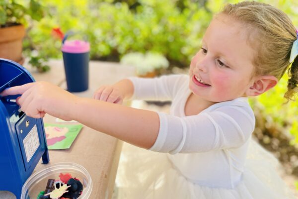 A photo of a little girl putting things in a toy mailbox and a container of small toys in front.