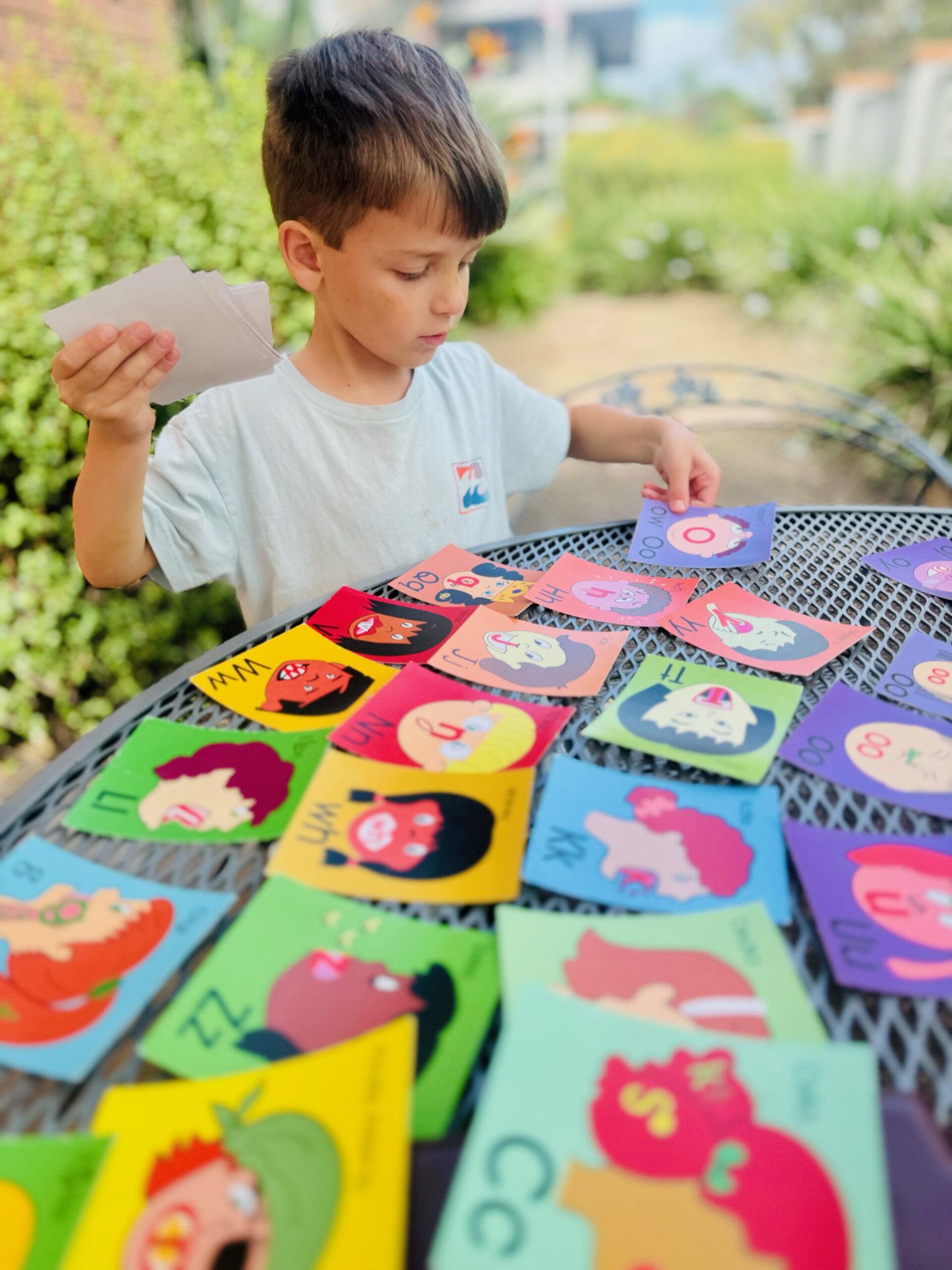 Boy in a t shirt sorting sounds cards on a table outside.